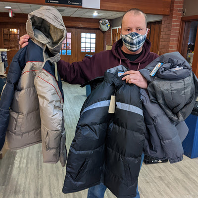 A person holding three winter jackets.