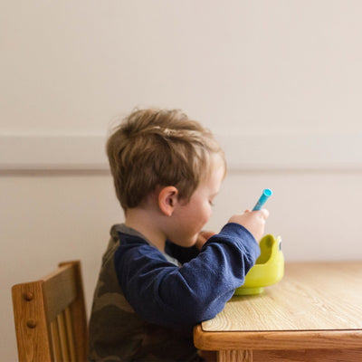 A child eating out of a bowl at a wooden table.