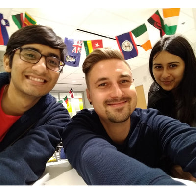 Three students sitting in front of a streamer of world flags.