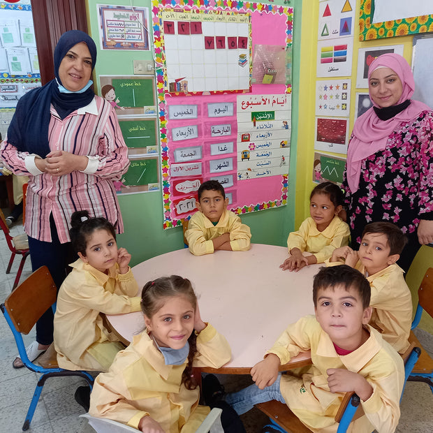 Two adults and a group of children sitting at a table in a classroom.