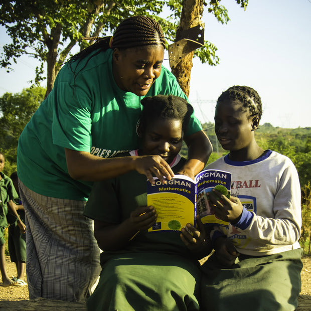 An adult and two youth reading a book outside.