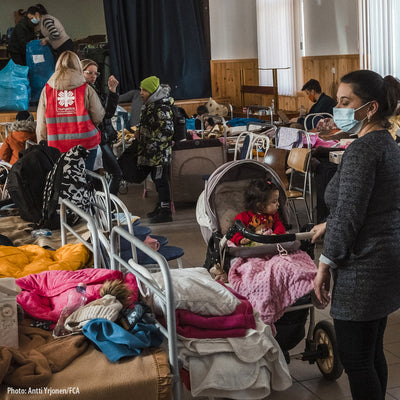 Aid workers in an bed-filled room, while adults and children wait for assistance.