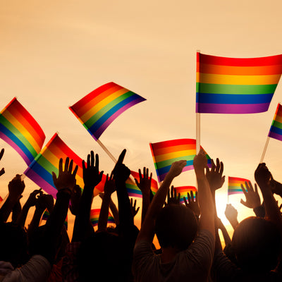 Hands holding up multiple rainbow flags.